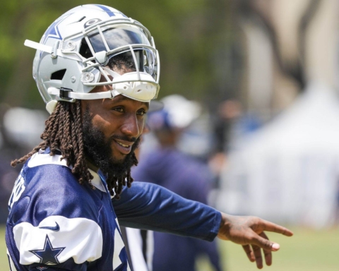 A football player in a Cowboys uniform and helmet points while standing outdoors during practice.