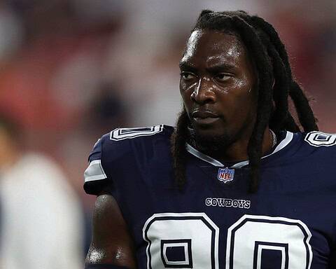 A football player in a navy blue "Cowboys" jersey with the number 90 is seen standing on the field.