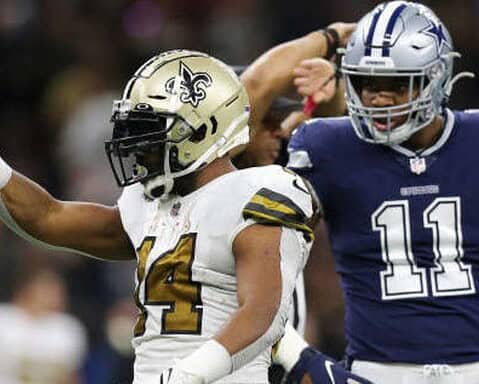 A Saints football player in a white and gold uniform celebrates while a player in a blue uniform stands in the background.