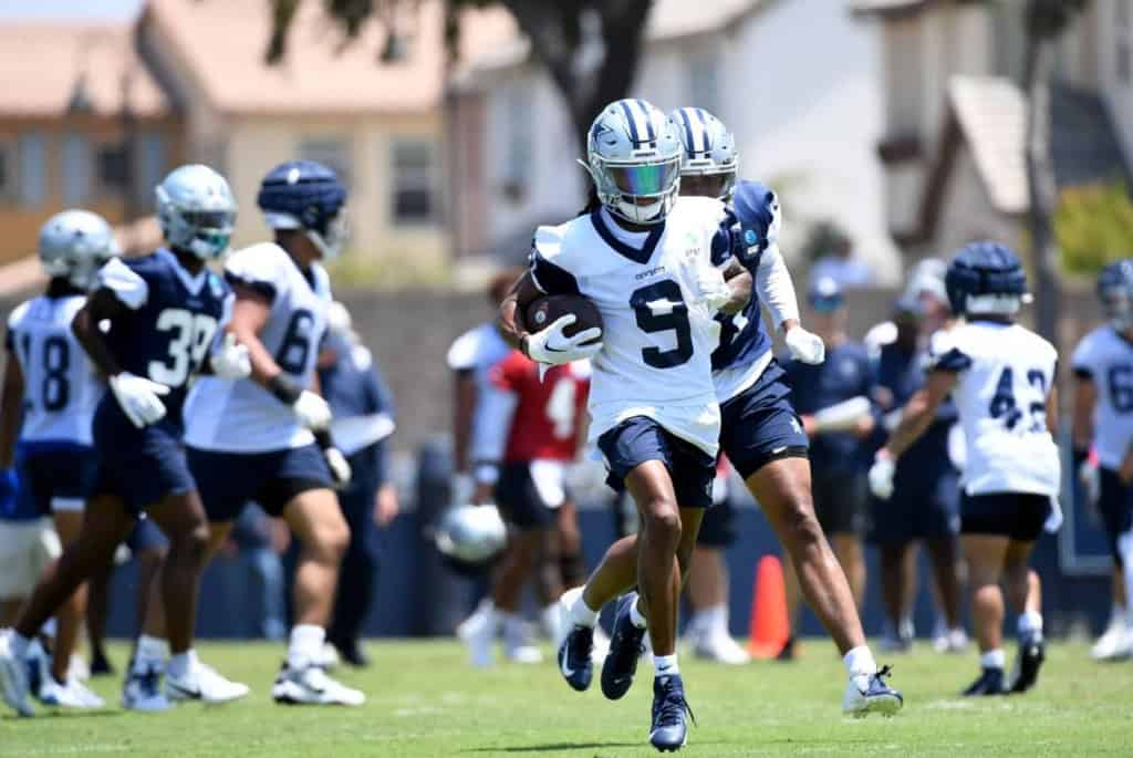 KaVontae Turpin and his fellow football players, clad in practice uniforms, engage in an intensive training session on a grassy field.