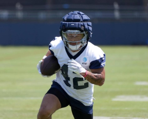 Cowboys' Deuce Vaughn, in training gear, runs with the football during a practice session on the grass field.