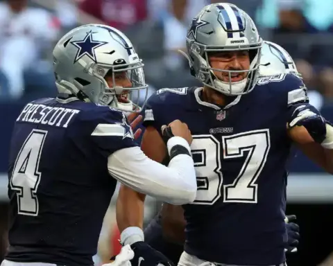 Two football players in blue uniforms celebrate on the field during a game, channeling the dynamic energy of Dak Prescott and Jake Ferguson.