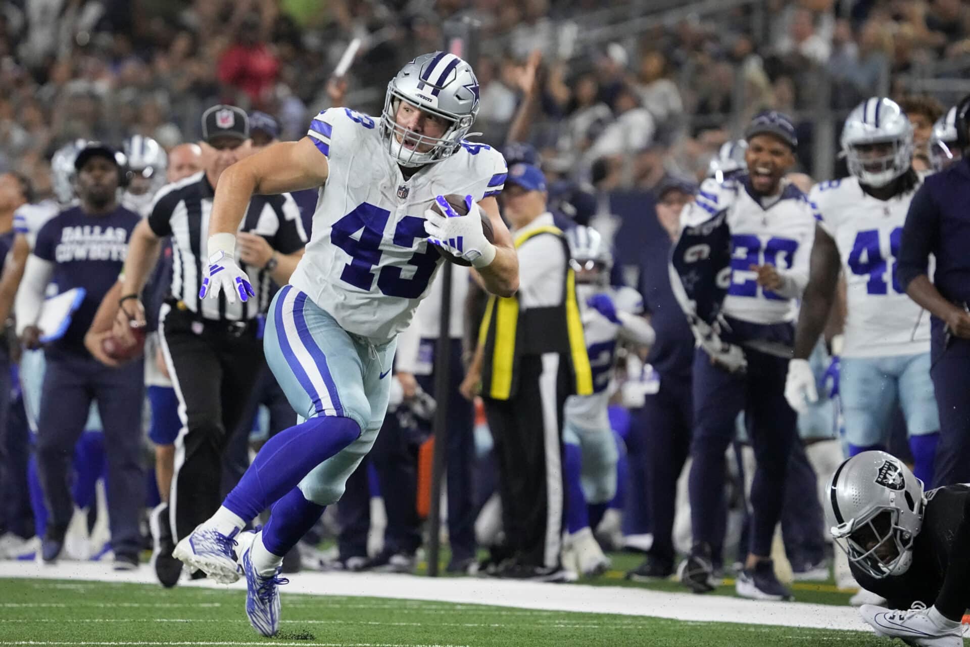 Hunter Luepke, in his Cowboys uniform, charges down the field with the ball, while both teammates and 49ers opponents focus on every move.