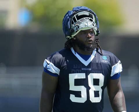 Football player in navy and white gear and helmet, numbered 58, stands on the field with a focused expression.