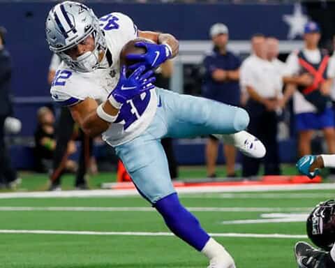 Cowboys football player Deuce Vaughn in blue and white uniform running with the ball, with defenders attempting to tackle him on the field.