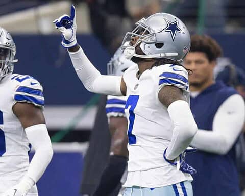 Two football players in Dallas Cowboys uniforms, including cornerback DaRon Bland, with one pointing upwards during a game.