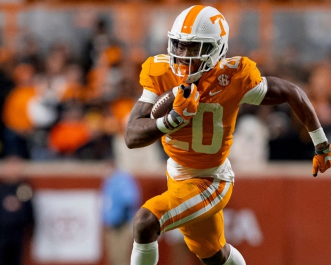 Jaylen Wright, a football player in an orange and white uniform, is seen running with the ball on the football field during a game.