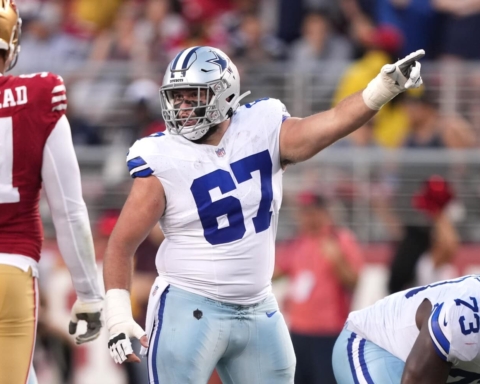 Dallas Cowboys player in a white uniform points during a game against the San Francisco 49ers, signaling to teammate Brock Hoffman.