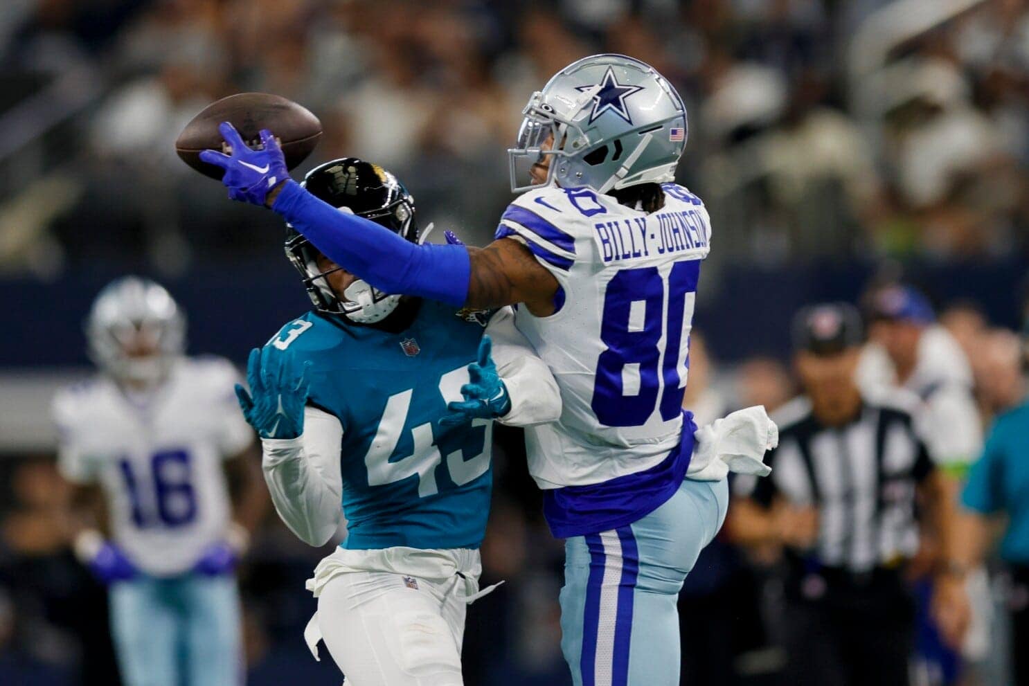 A football player in a blue uniform attempts to catch a pass, while Tyron Billy-Johnson, in a white and blue uniform, tries to block him.