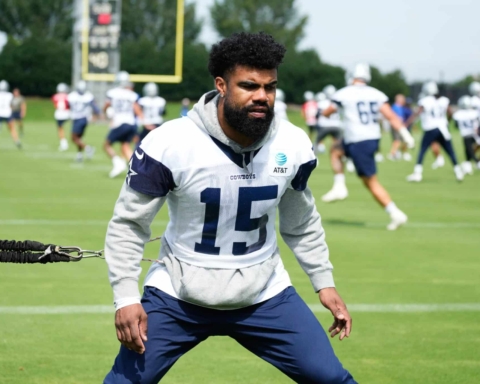 Football player training on a field with teammates in the background during a practice session.