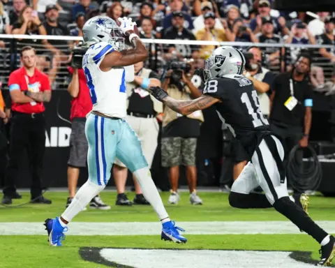 Dallas Cowboys player catching a football while being defended by a Las Vegas Raiders player during a game.