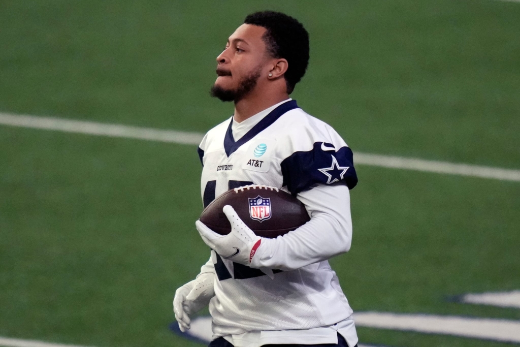 A football player in a white jersey holding a football on a field during a practice session.