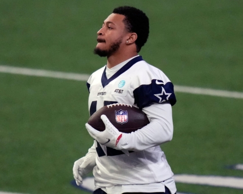 A football player in a white jersey holding a football on a field during a practice session.