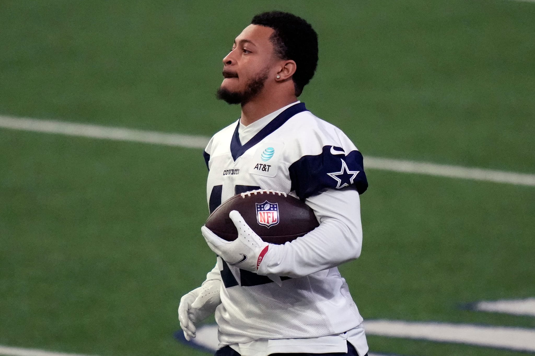 A football player in a white jersey holding a football on a field during a practice session.