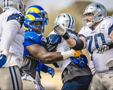 Football players from two teams in blue, white, and yellow uniforms engaged in a heated altercation during a Cowboys vs Rams practice game.
