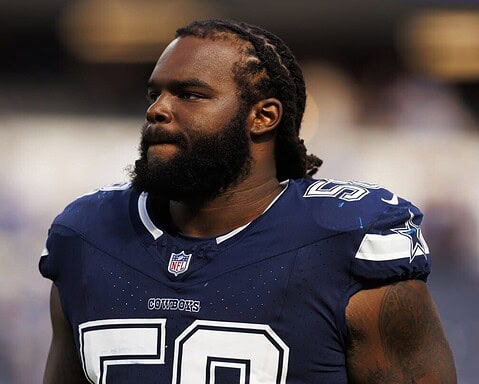 A football player in a Dallas Cowboys jersey stands on the field with a focused expression.