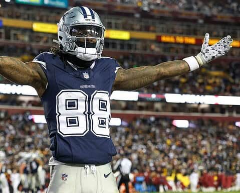 Football player wearing a Dallas Cowboys uniform with arms outstretched on the field during a game.