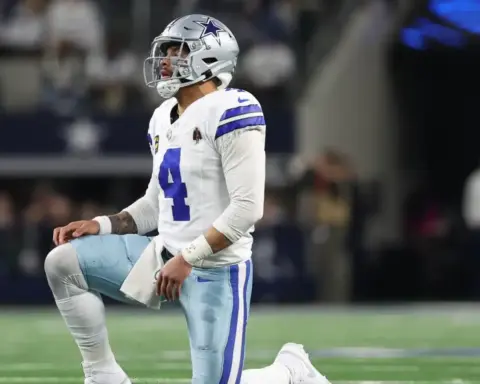 Football player in Dallas Cowboys uniform kneels on the field during a game.