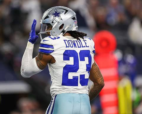 Football player in a white and blue uniform with the name "Dowdle" and number 23 on the jersey, raising his left hand.