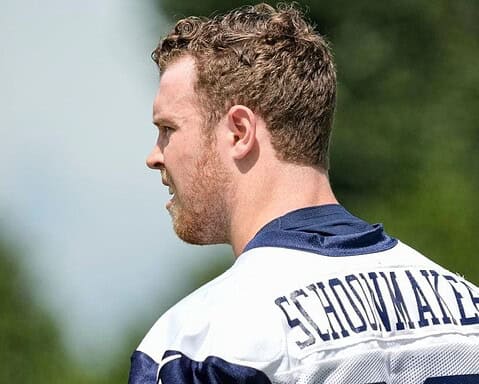 Man in a football jersey with the name "Stidham" on the back looking to the left, with a blurred green background.