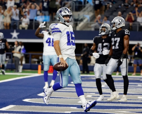 Trey Lance, donning blue and white, charges down the field to score a touchdown as the players in black and white look on.