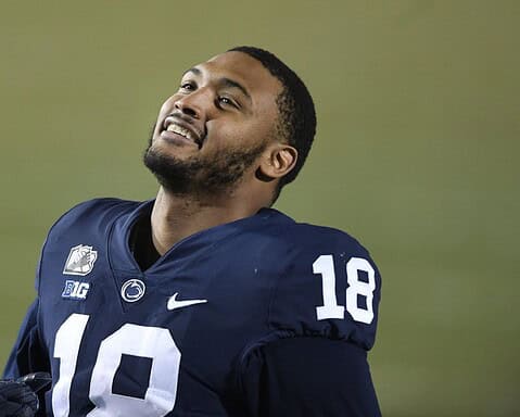 A football player in a blue jersey, number 18, looks up and smiles during a game, reminiscent of the joy seen when the Cowboys sign 2 defensive ends.