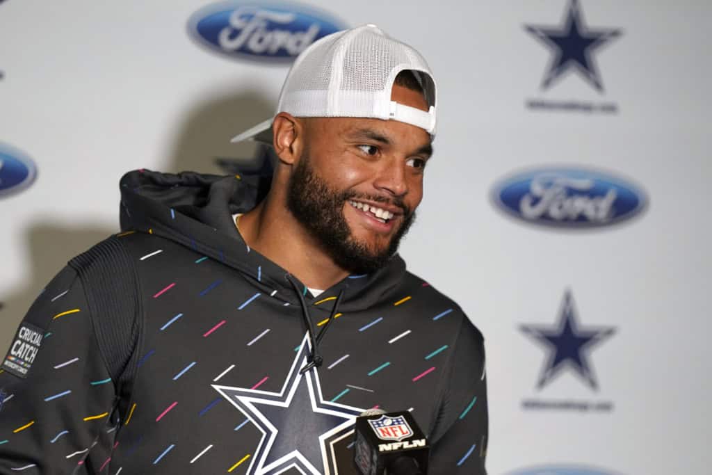 A man in a hoodie and cap stands in front of a backdrop with Ford and Dallas Cowboys logos, smiling.