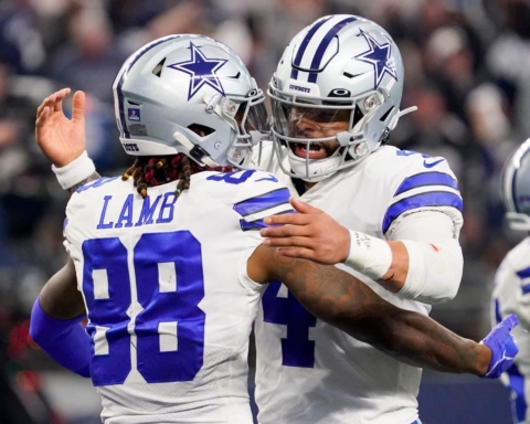 Two football players in Dallas Cowboys uniforms embrace on the field during a game.