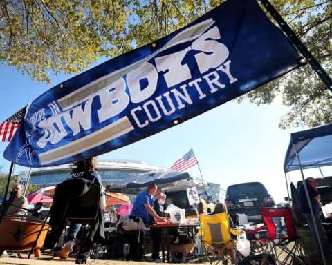 People tailgating under a "Cowboys Country" banner, with American flags and camping equipment visible in the background.