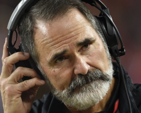 Man with a thick white beard, wearing headphones and adjusting the left earpiece.