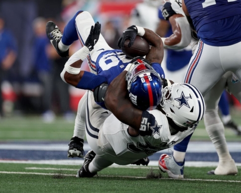 A football player in white tackles another player in blue, bringing him to the ground during a football game.