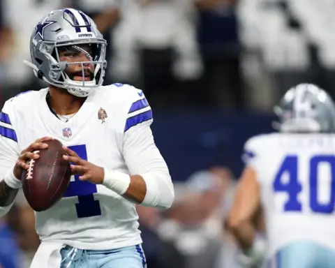 Football player in a white Dallas Cowboys uniform holding a football, preparing to throw during a game.
