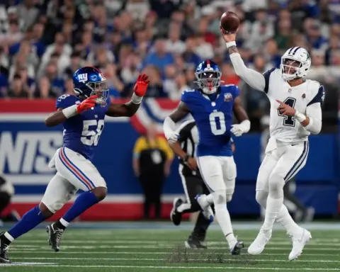 Football player throwing a pass while being pursued by a defender in a stadium filled with spectators.