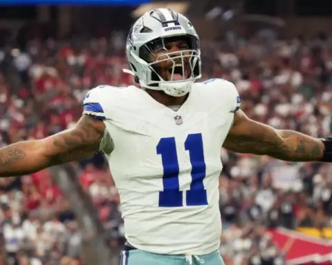 Football player in a white and blue uniform celebrates on the field with arms outstretched during a game.