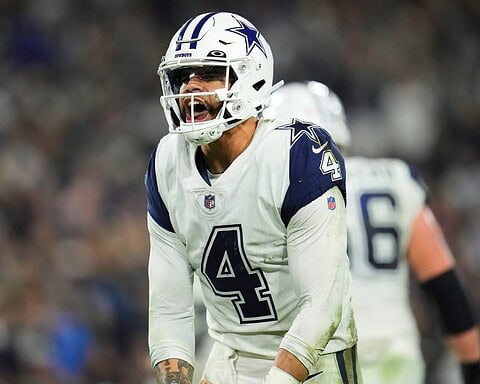 A football player wearing a Dallas Cowboys uniform and helmet appears to be shouting during a game.