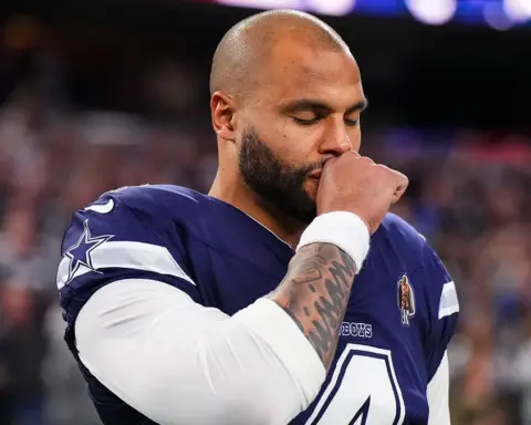 Football player in a navy jersey stands with eyes closed and hand to face on a field during a game.