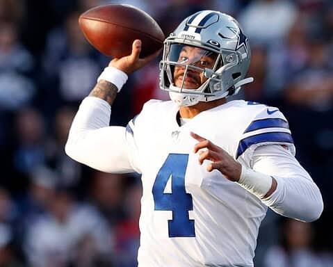 Football player wearing a Dallas Cowboys uniform preparing to throw a football during a game.
