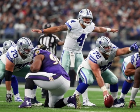 Football players from the Cowboys and Ravens are positioned pre-snap on the field during a game.