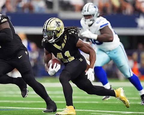 Football players from two teams in action on the field, one holding a football and running with teammates nearby.