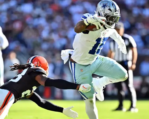 A football player in a white uniform dodges a tackle from an opponent in a black uniform during a game.