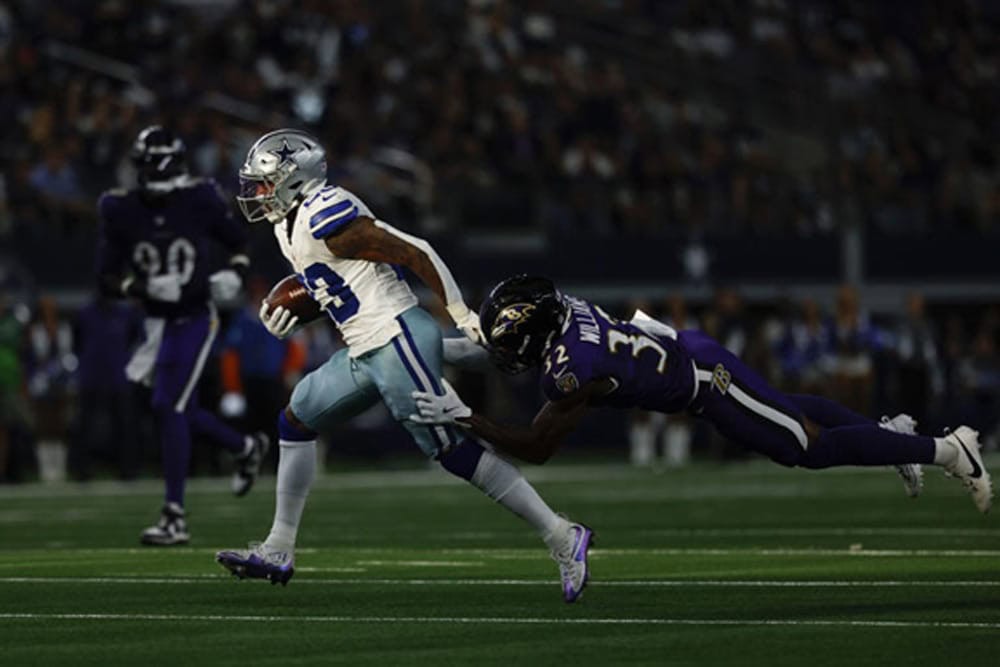 A football player in a white uniform is tackled by a player in a purple uniform during a game.