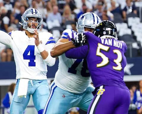 A quarterback prepares to throw the football while teammates block defensive players during a game.