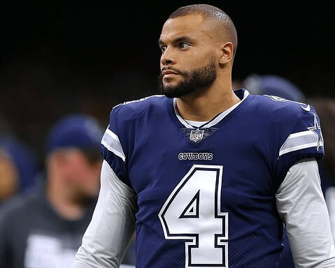 A football player in a blue Cowboys jersey with number 4 stands on the field.