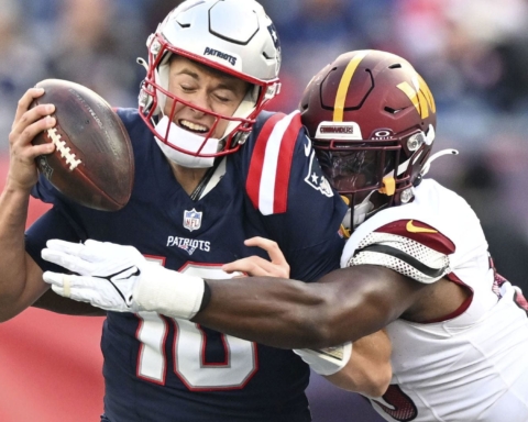 Football player in blue jersey being tackled by opponent in white and maroon jersey during a game.