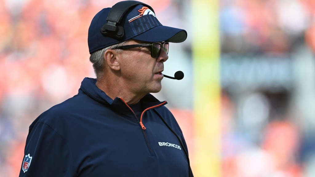 A man wearing a Broncos cap and headset stands on the sports field, ready to contribute to the offensive strategy.