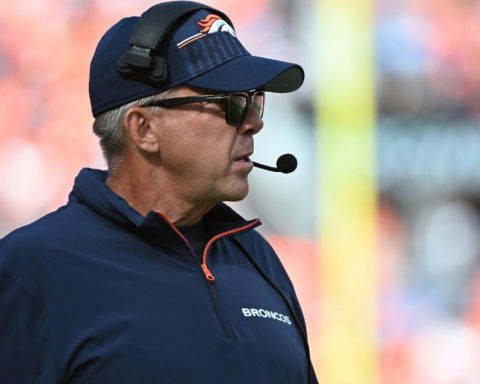 A man wearing a Broncos cap and headset stands on the sports field, ready to contribute to the offensive strategy.