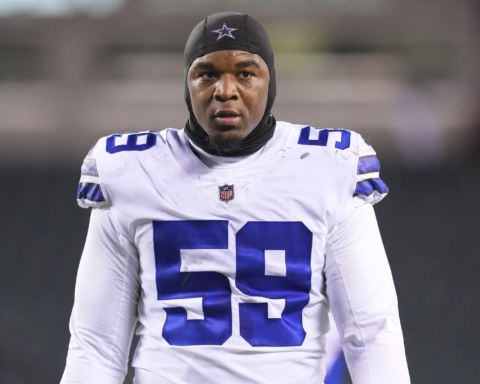 Football player wearing a Dallas Cowboys jersey and headgear, standing on a field.