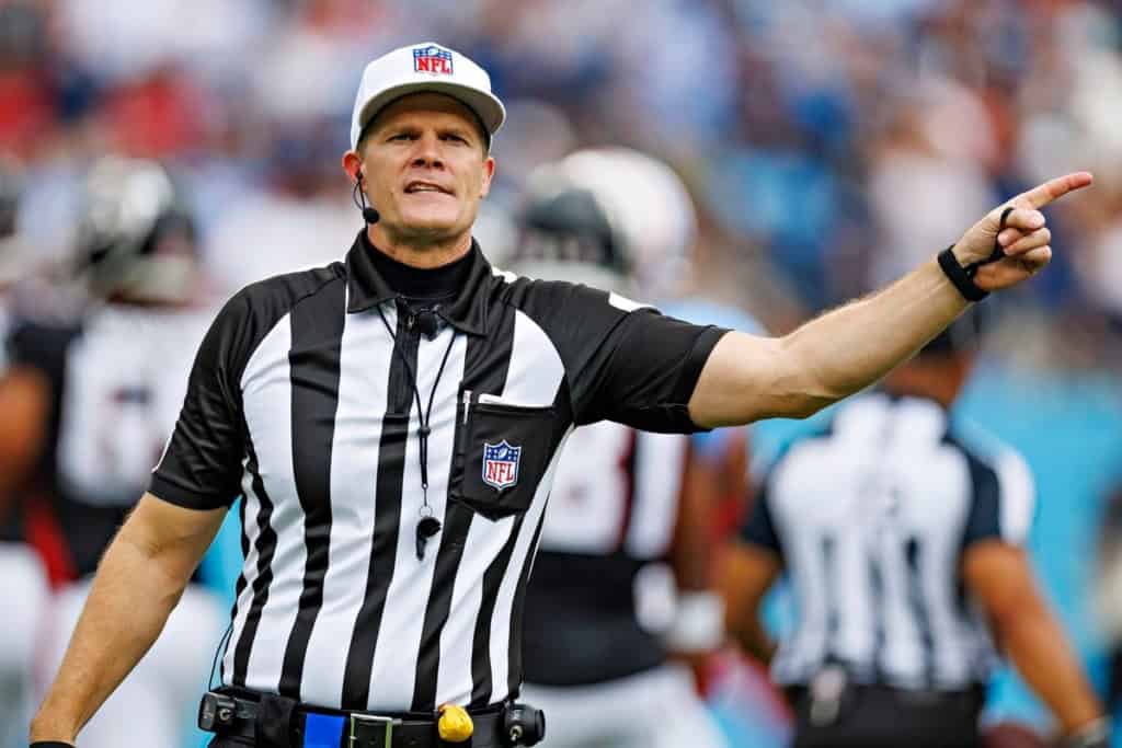 Referee in a football game making a call, wearing striped uniform and cap, pointing with his right arm.