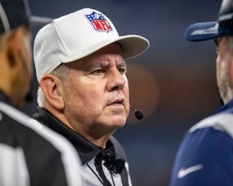 A football referee in conversation with two coaches on the field.