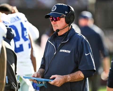 A football coach for the Cowboys, sporting sunglasses and a headset, looks at a tablet on the sidelines during a game this season.